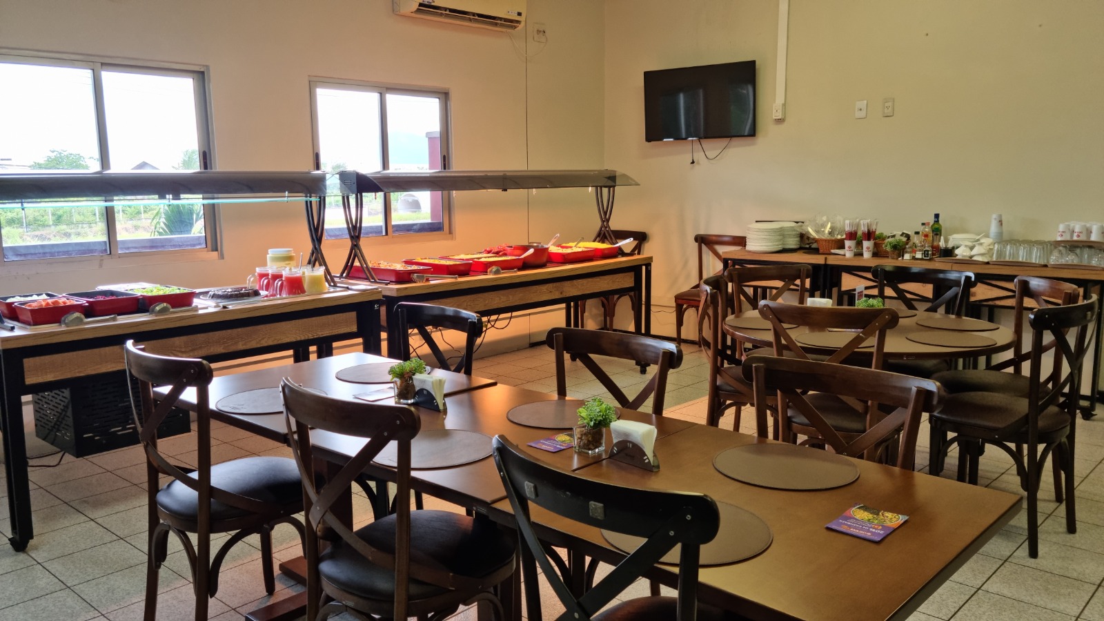Ambiente interno do Santé com mesas de madeira e buffet ao fundo próximo às janelas.